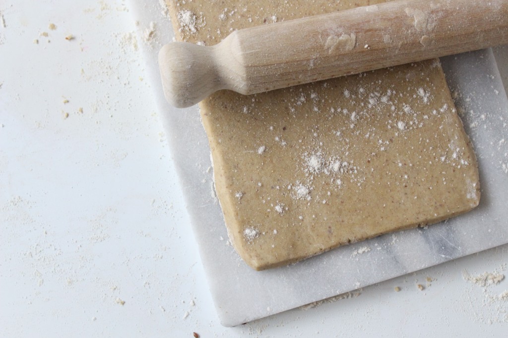 Overhead shot of gluten free pastry rolled out into a rectangle on a marble board. A wooden rolling pin is resting on top. 