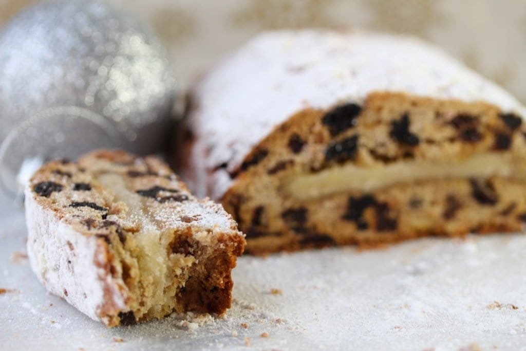 A slice of stollen laying on it's side showing the middle layer of marzipan. The remainder of the loaf is in the background. 