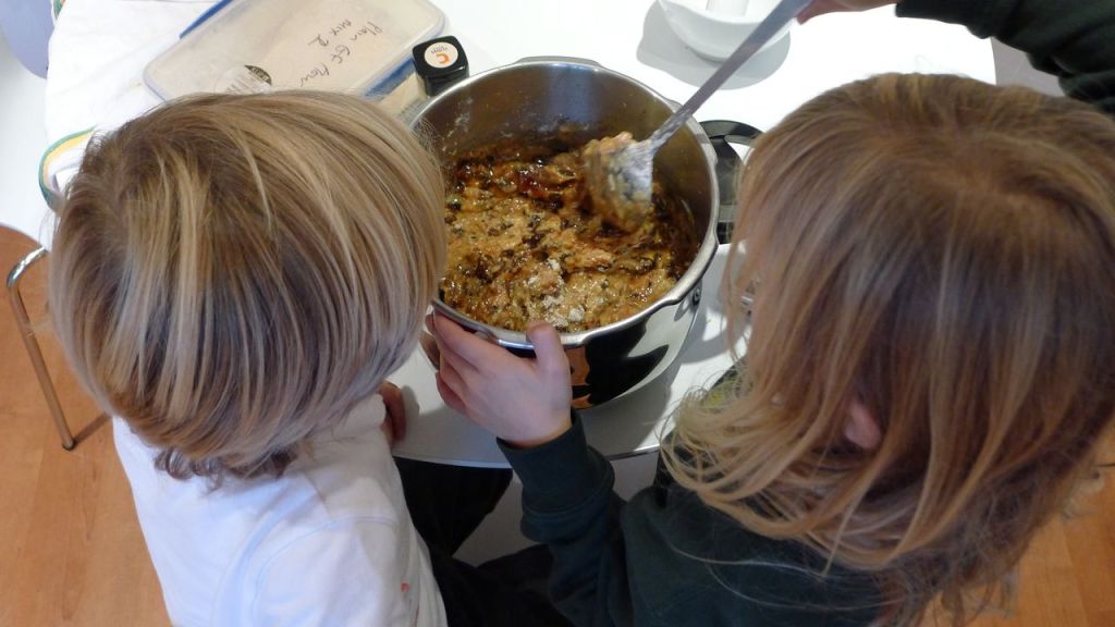 Overhead shot of two children mixing the cake batter together in a silver bowl. 