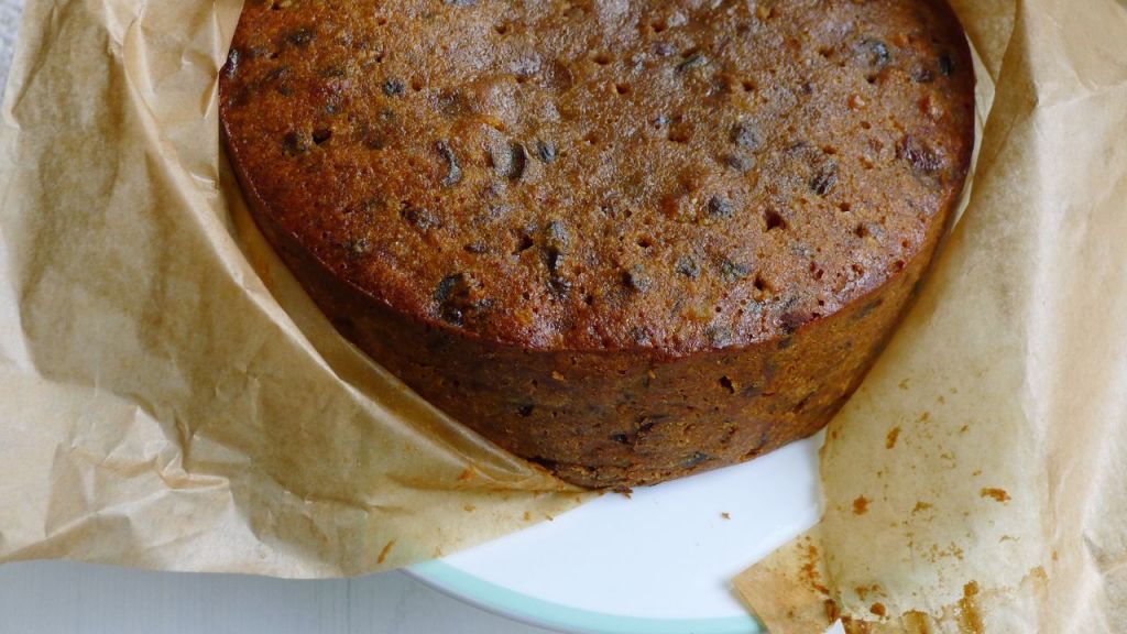 A whole undecorated Gluten Free Christmas Cake shown partially wrapped in parchment paper. 