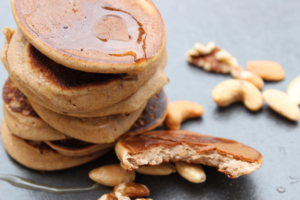 A stack of flourless banana pancakes on a black board with nuts scattered around.