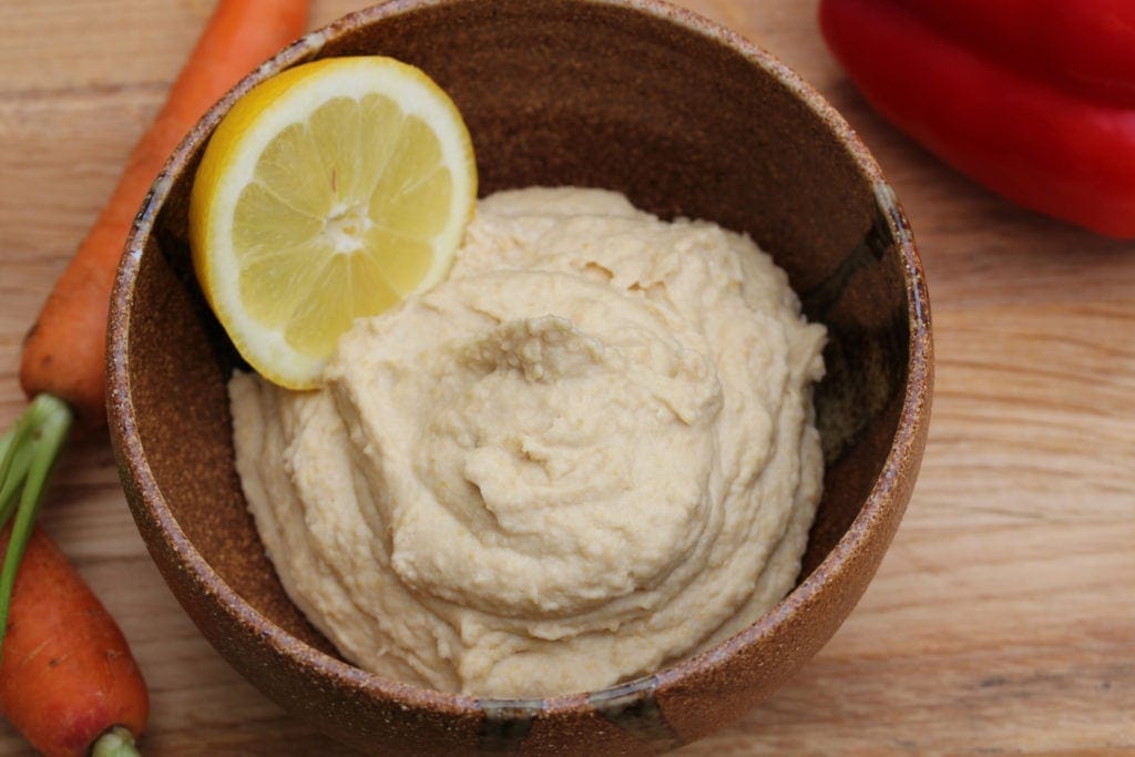 A bowl of lemon hummus with a slice of lemon