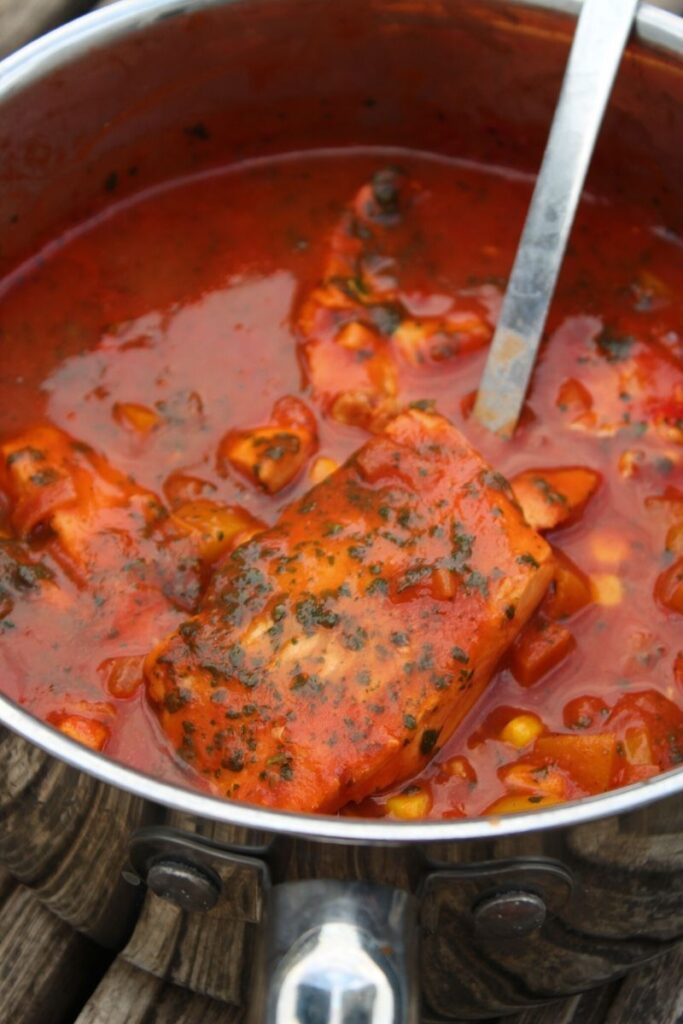 Fillet of fish in a spicy tomato sauce with a large metal spoon in the pan. A Moroccan fish recipe.