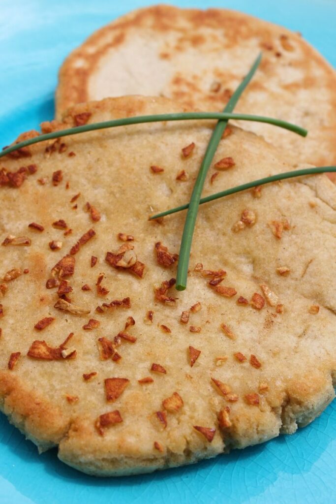 Portrait photograph of two gluten free garlic bread flatbreads on a blue plate with green chives scattered on top.