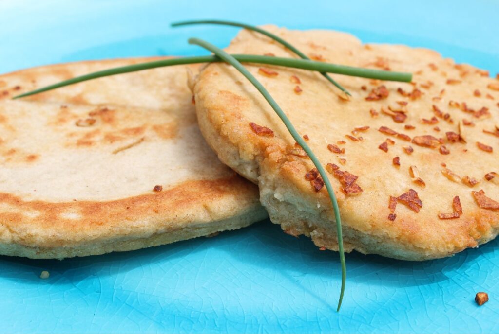 A side view of two gluten free garlic flatbreads on a blue plate. Crispy garlic pieces on top and on the plate.