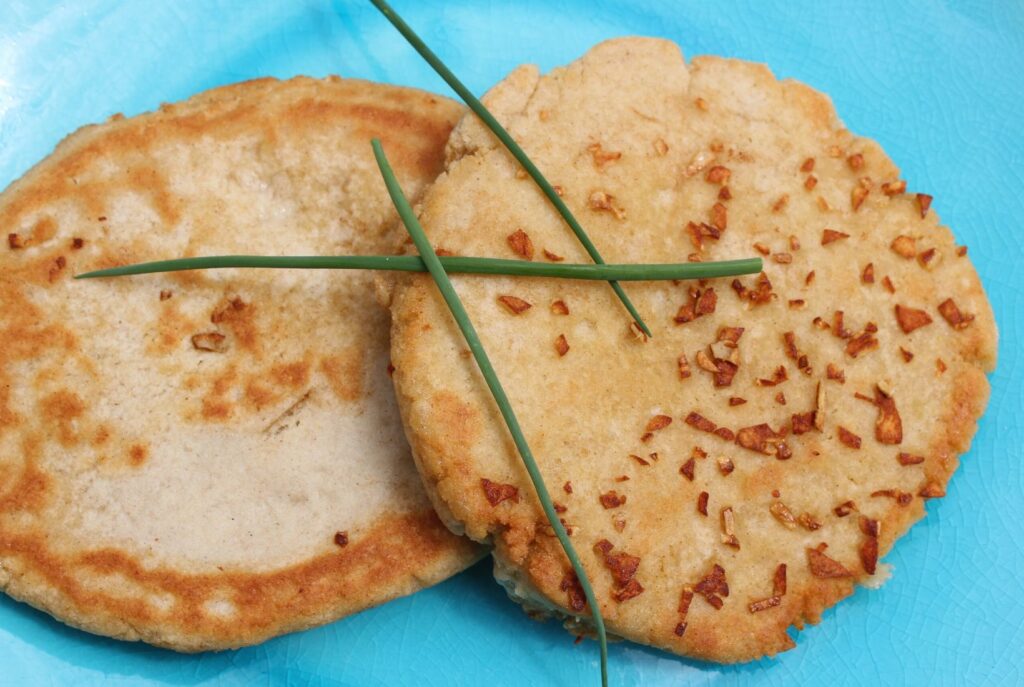 Two gluten free garlic bread flatbreads lying on top of one another with pieces of chive across the top.