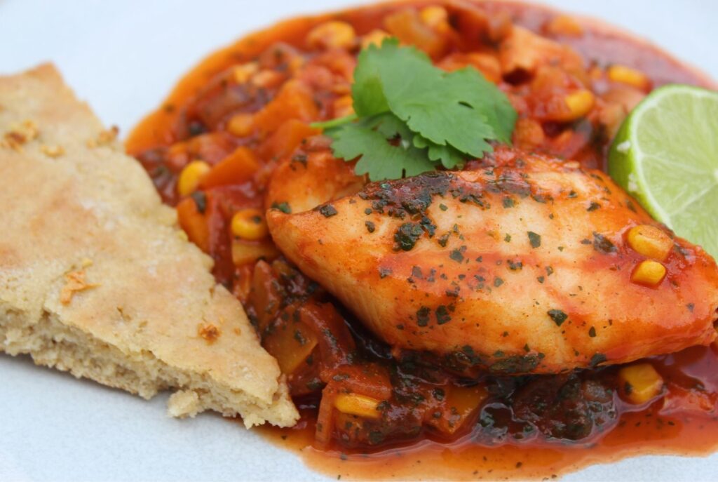 Moroccan fish - a spicy tomato sauce with frozen fish - served on a white place with a slice of garlic bread.