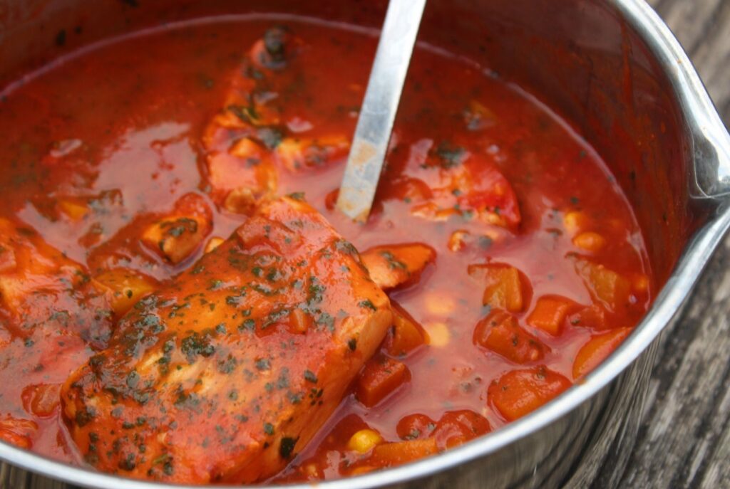 A Moroccan fish recipe in the pan with spicy red sauce and specks of coriander showing.