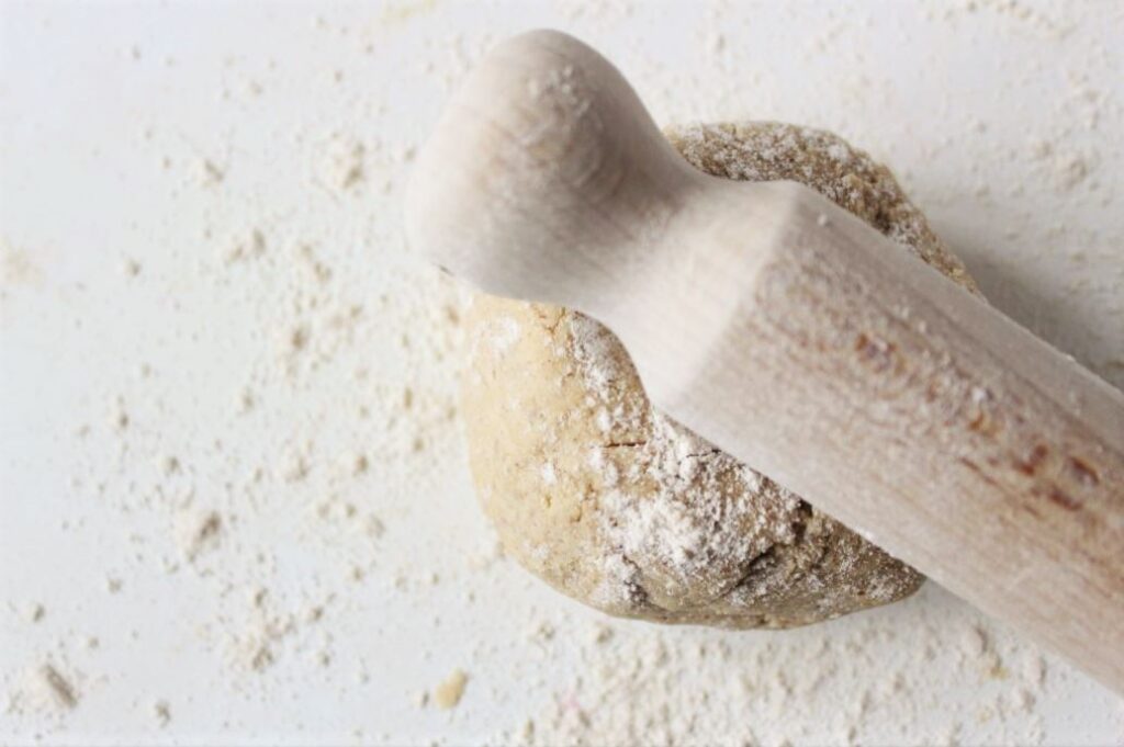 Ball of pastry on a floured white surface with a rolling pin on top ready to be rolled. 