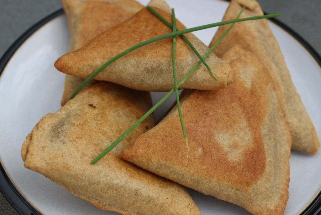 Gluten free samosas on a white plate with black rim, scattered with chives