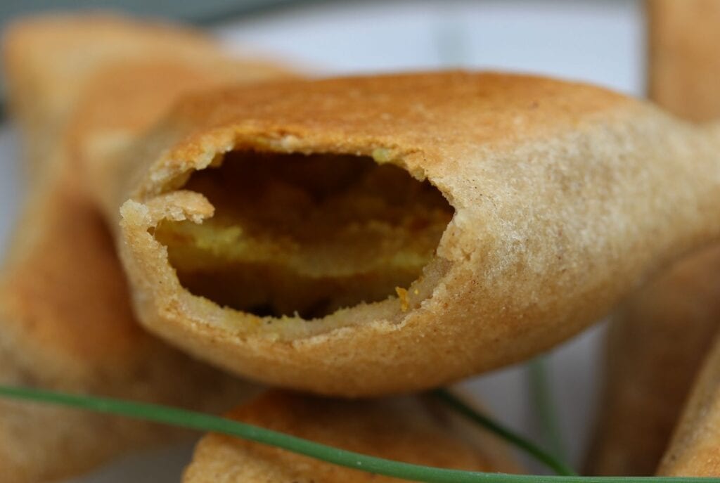 A close up view of the gluten free samosa with a bit taken out, showing the filling of potato and spices.