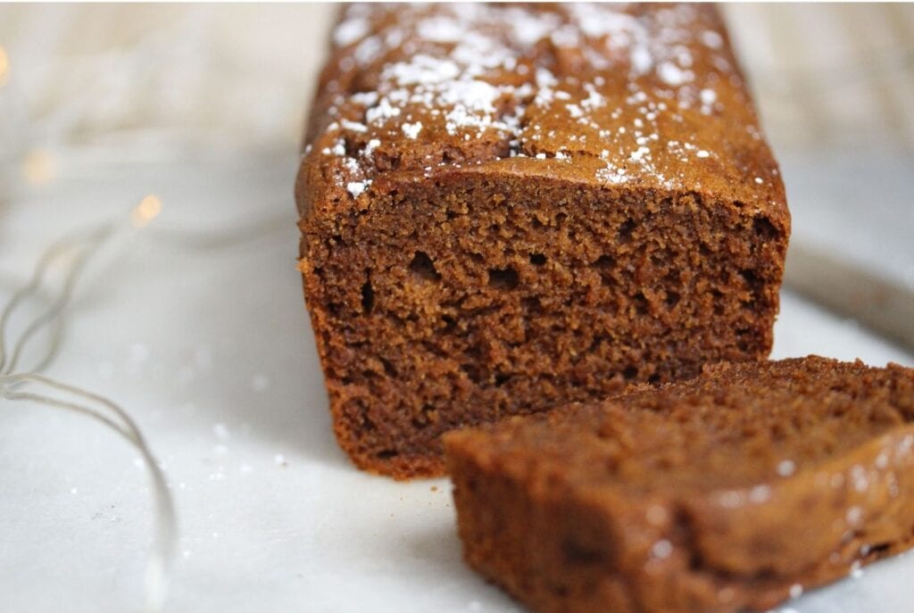 Gluten free gingerbread sliced open with a slice on one side and the whole cake on the other