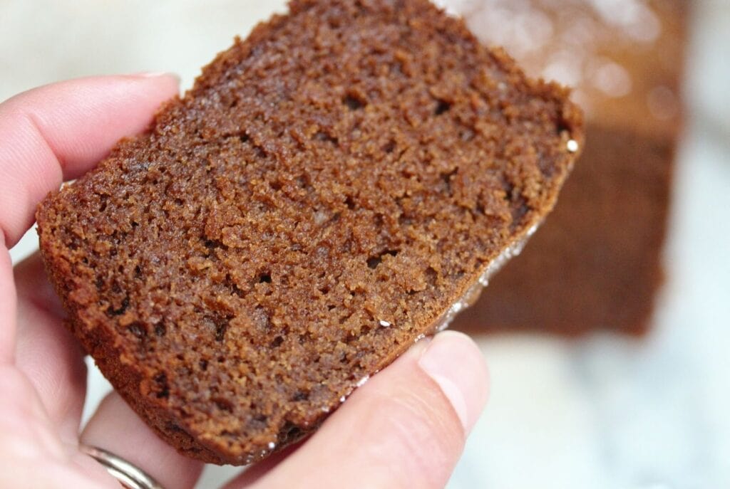 A slice of gluten free ginger cake held in a hand showing a lovely moist, sticky texture