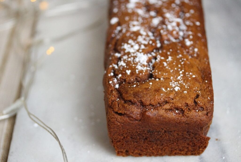 Gluten free ginger cake with a scattering of icing sugar on top and some pretty fairy lights to the side.