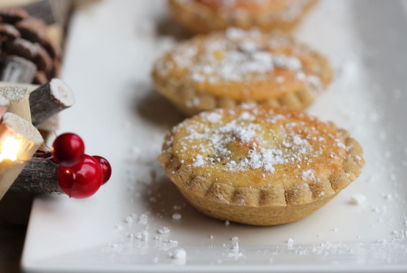 gluten free mince pies with a frangipane topping shown on a white plate with Christmas decorations to the left.