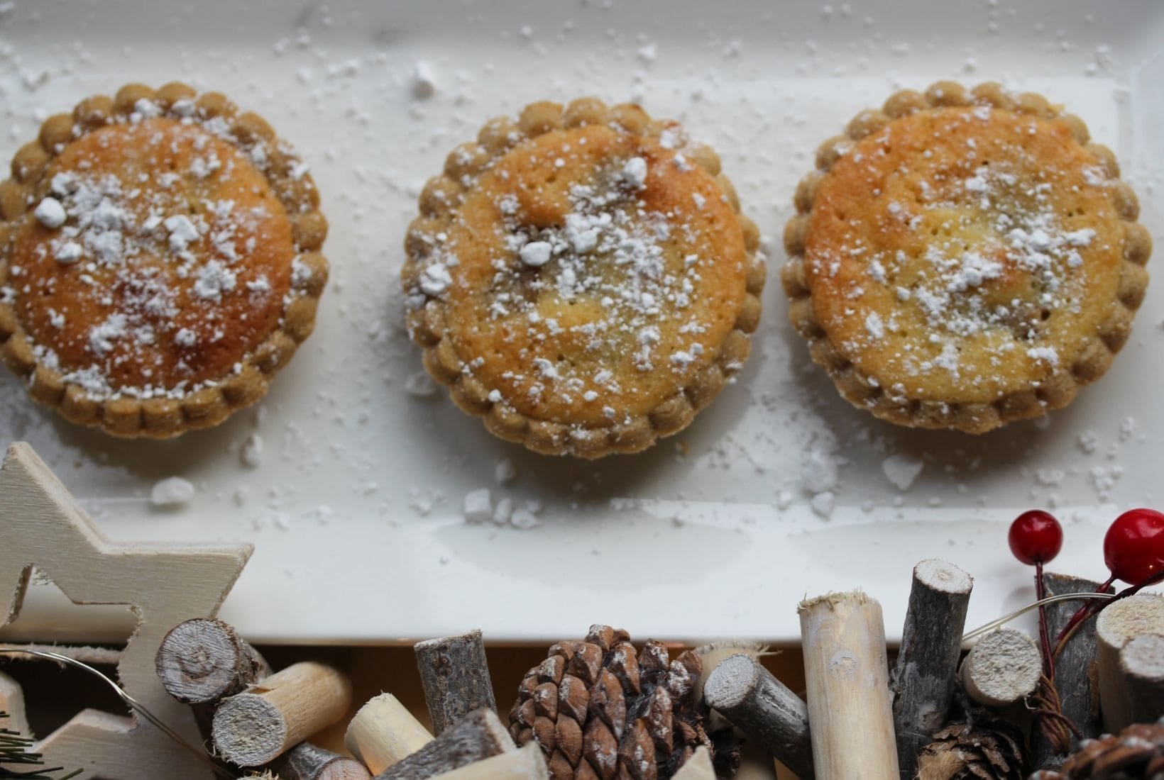 3 gluten free frangipane topped mince pies on a white plate with Christmas decorations